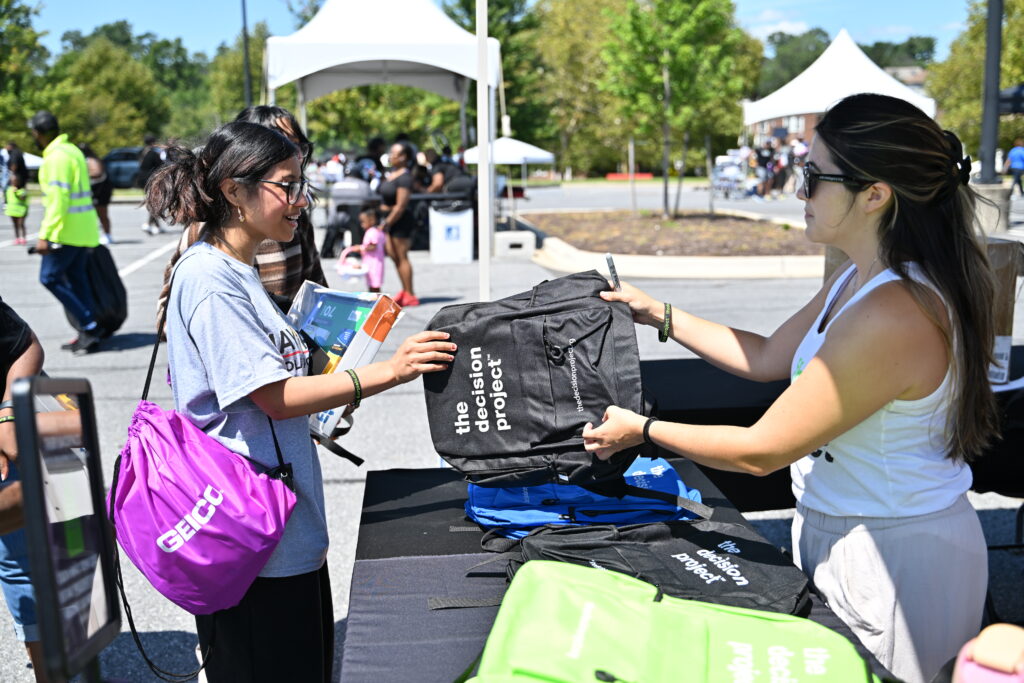 A community outreach team member hands out The Decision Project backpacks to students at a local block party.
