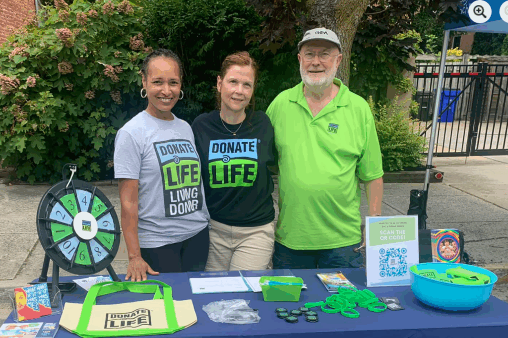 Three volunteers stand at an Infinite Legacy booth to hand out Donate Life merchandise to encourage organ, eye and tissue donation.