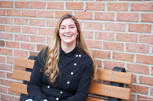 Director, Business Intelligence, Tiffany Arrington, sits on a bench outside of Infinite Legacy's office smiling.